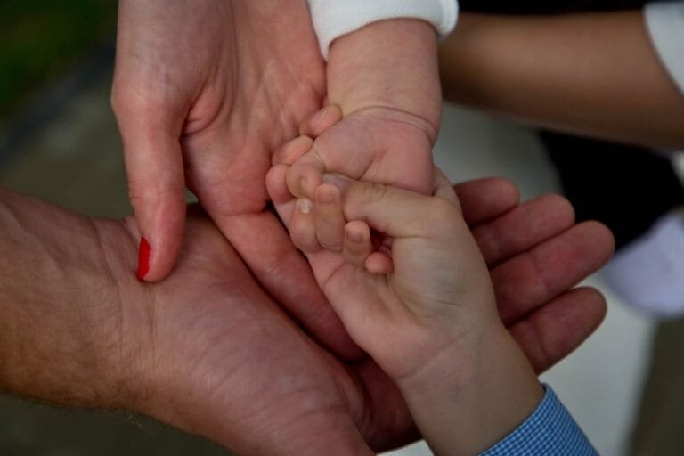 Como podemos ajudar? 7 Close-up of a family joining hands, symbolizing love and connection.