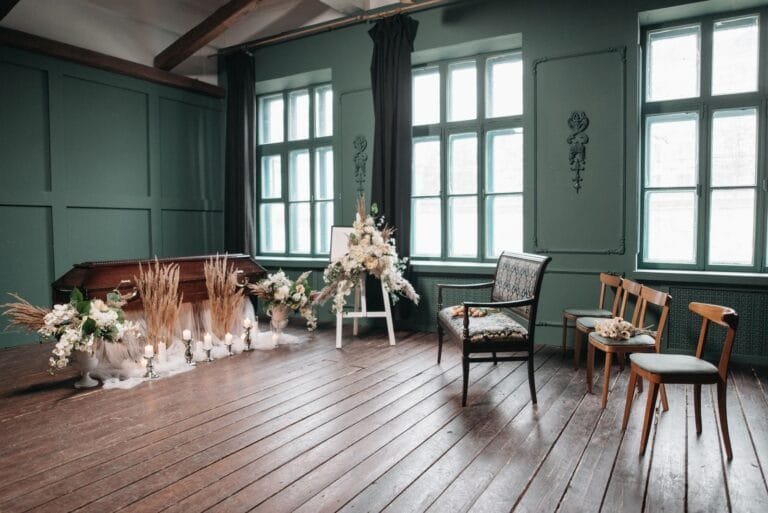 Pensão por Morte Presumida: Como Requerer Sem Certidão de Óbito 8 A serene funeral setup with a wooden coffin, chairs, and floral arrangements in a green room.