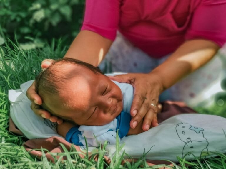 Pensão Vitalícia do INSS Beneficia Famílias Zika em 2026 3 A peaceful baby lying on the grass being gently cared for by a woman.