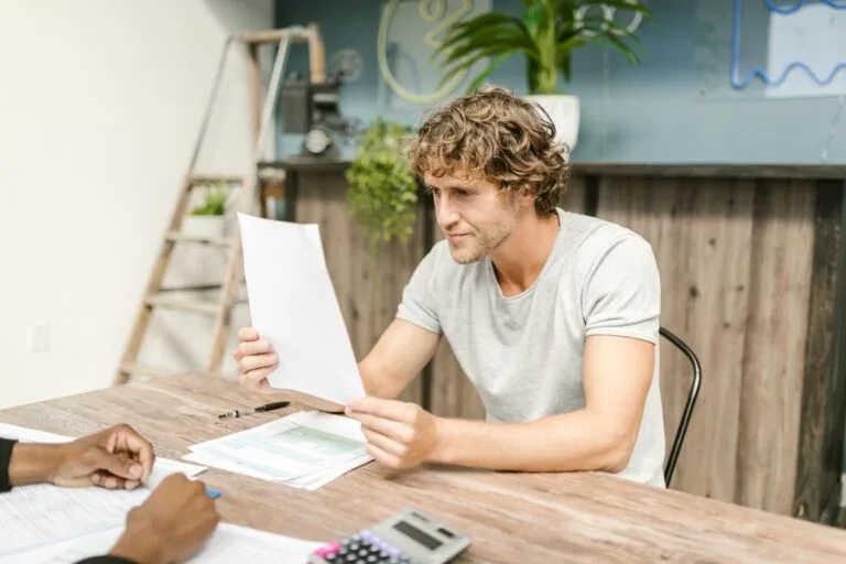 A man with curly hair evaluates documents at a desk, highlighting focused work in a profes