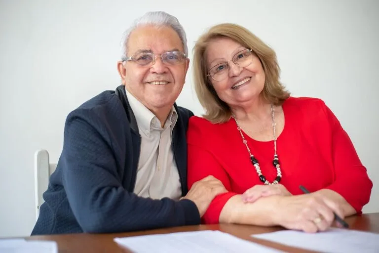 Planejamento SucessórioBenefícios e Estratégias Jurídicas 6 Elderly couple embracing and signing papers, sharing a warm and happy moment together.