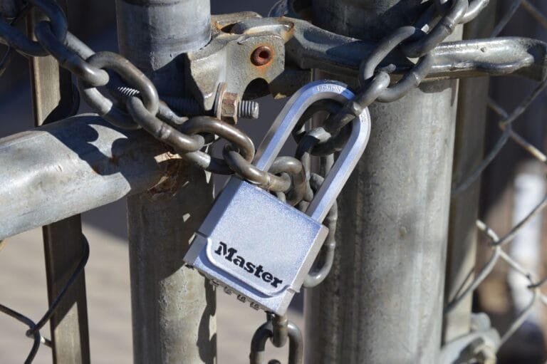 Detailed view of a padlock securing a metal gate with a chain, emphasizing safety and secu