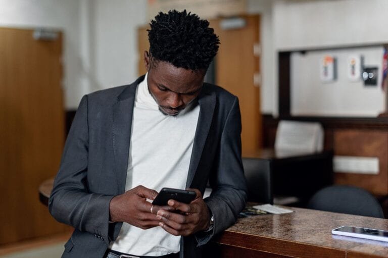Porto Grande (AP): INSS Amplia Serviços em 2026 6 Professional man leaning on a counter, focused on his mobile phone in a contemporary office setting.