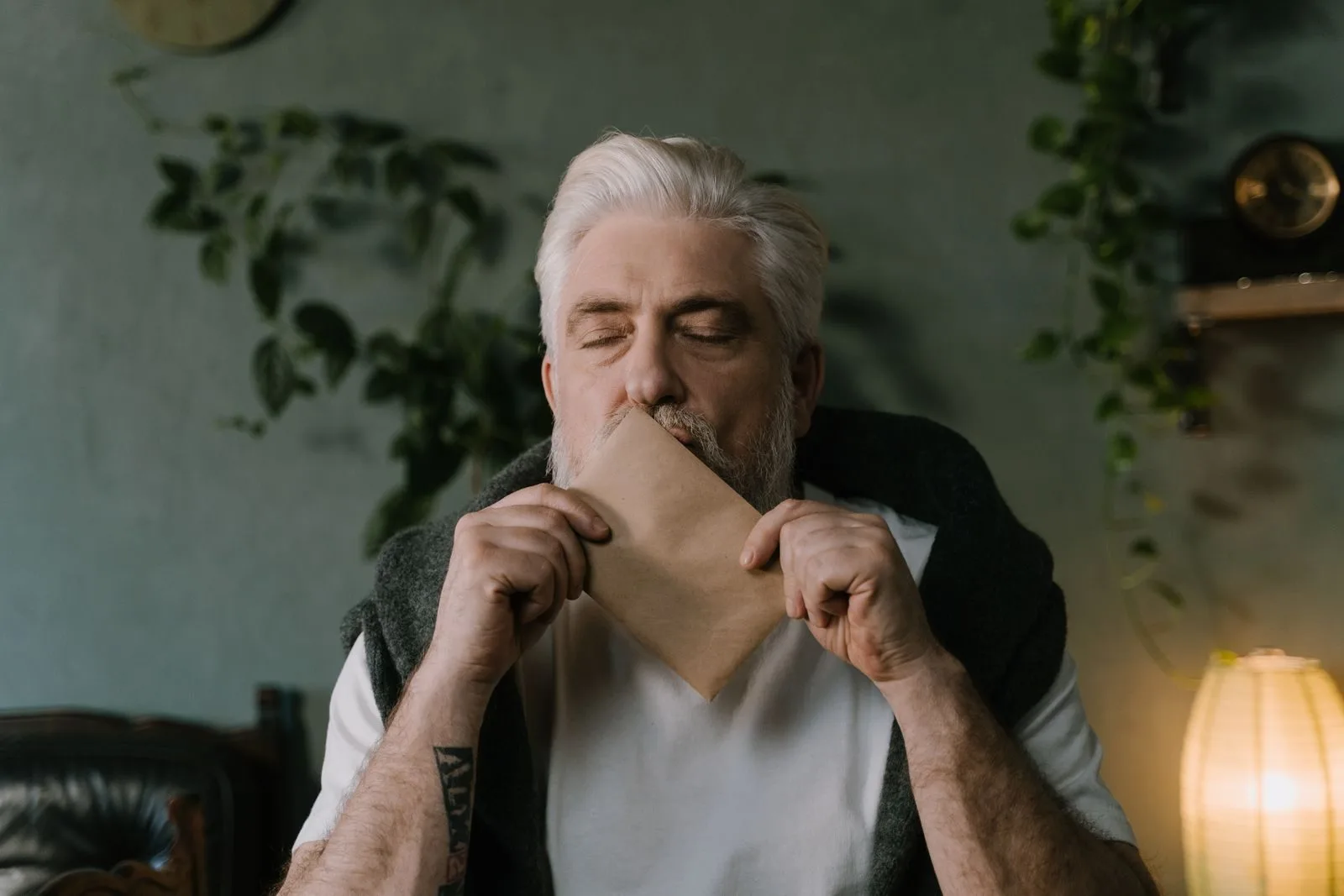 Elderly man holding an envelope, eyes closed, savoring a moment indoors.