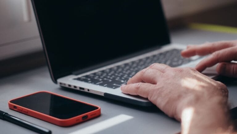 Processo eletrônico: como acompanhar o seu caso sem sair de casa 7 Close-up of hands typing on a laptop beside a smartphone. Ideal for tech and work themes.