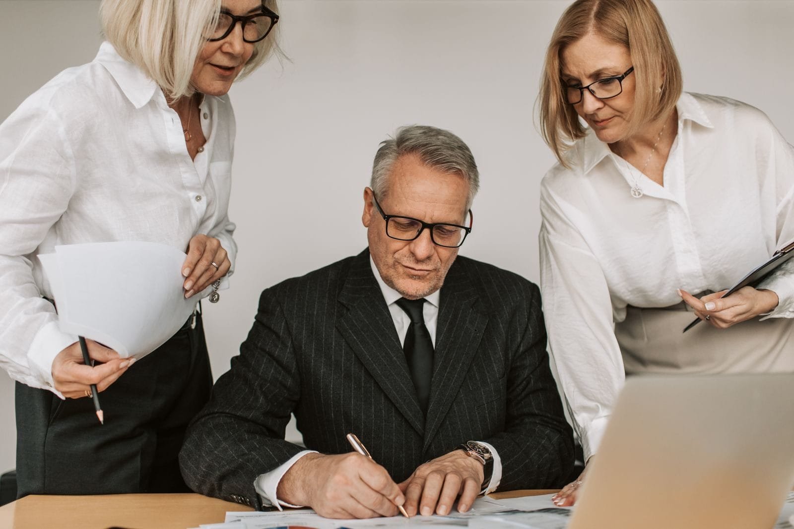 Senior professionals in an office setting reviewing and signing business documents together.