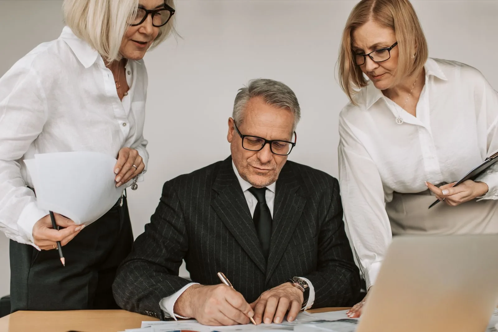 Senior professionals in an office setting reviewing and signing business documents together.