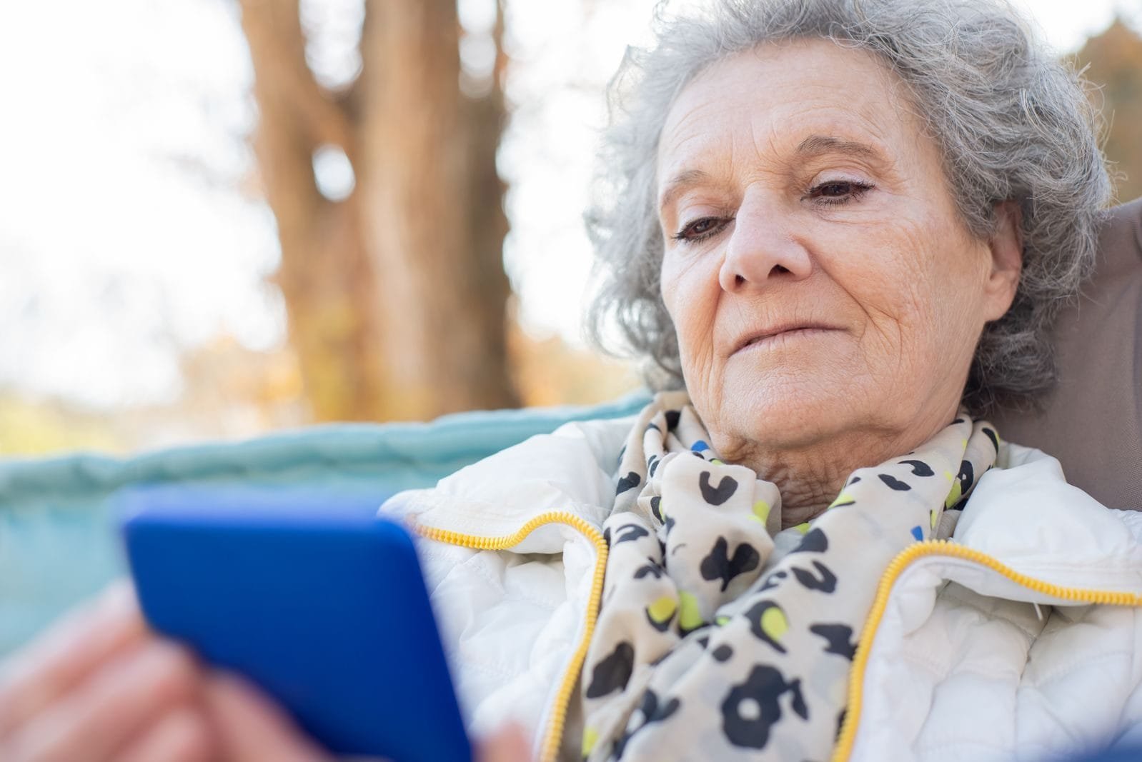 Prova de Vida INSS 2026: Prazo, Como Fazer e Consequências 1 Elderly woman with a smartphone relaxing outdoors in autumn.
