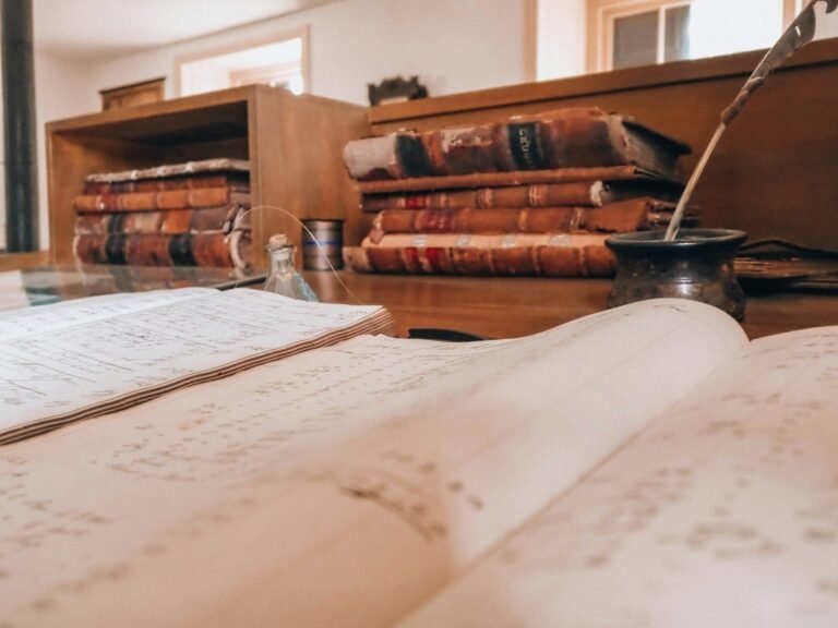 Open book, old books, and a quill on a desk.