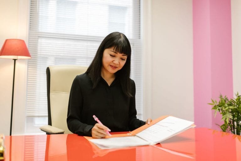 Asian woman working in a bright modern indoor office setting reviewing paperwork.