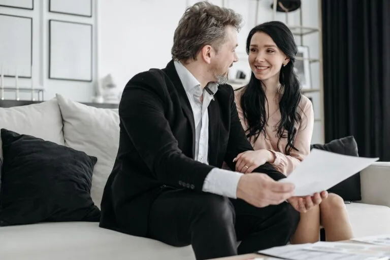 Couple smiling while sitting on a couch reviewing documents indoors.