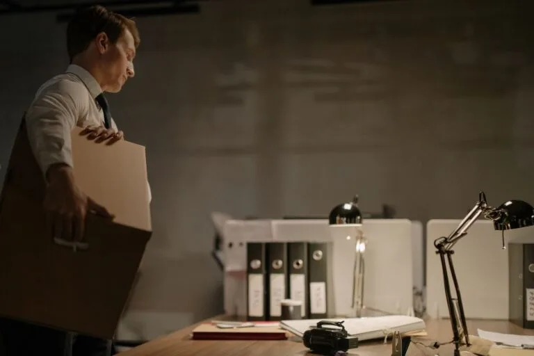 Remoção e Redistribuição de Servidor Público Federal 5 Businessman stands at desk packing documents in a dimly lit office setting.