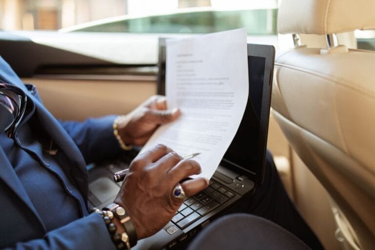 Como podemos ajudar? 13 A businessman reviews documents on a laptop while traveling in the backseat of a car.
