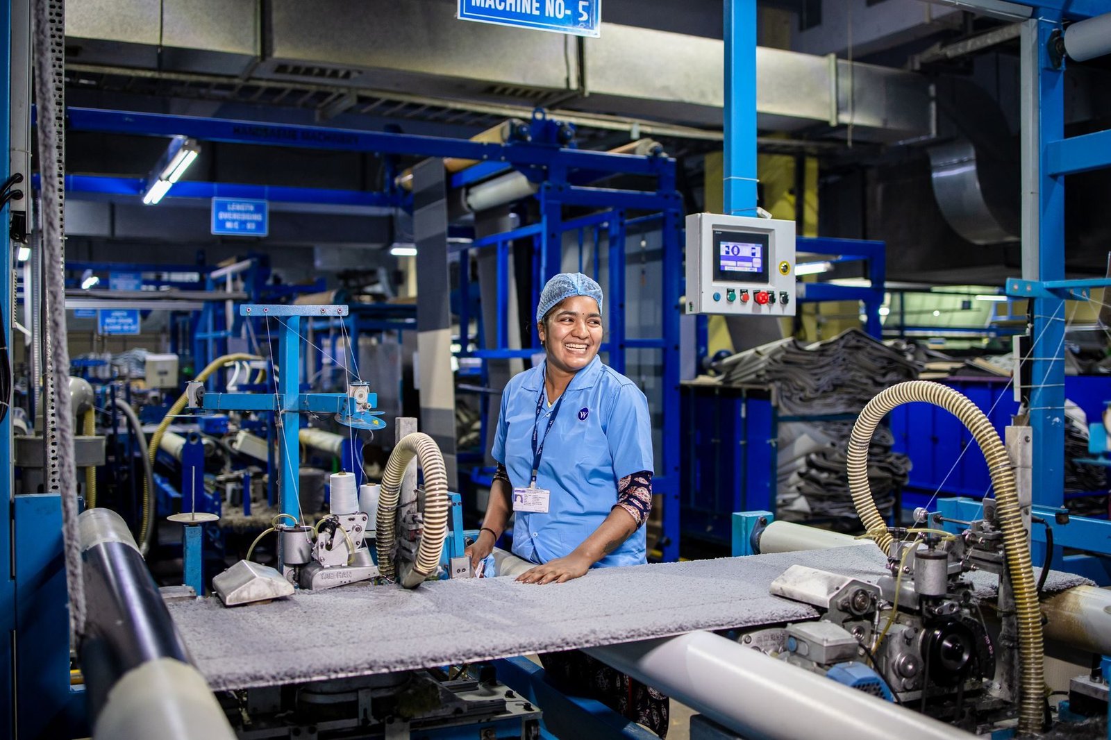 A blue-collar worker smiling while operating textile machinery in an industrial setting.