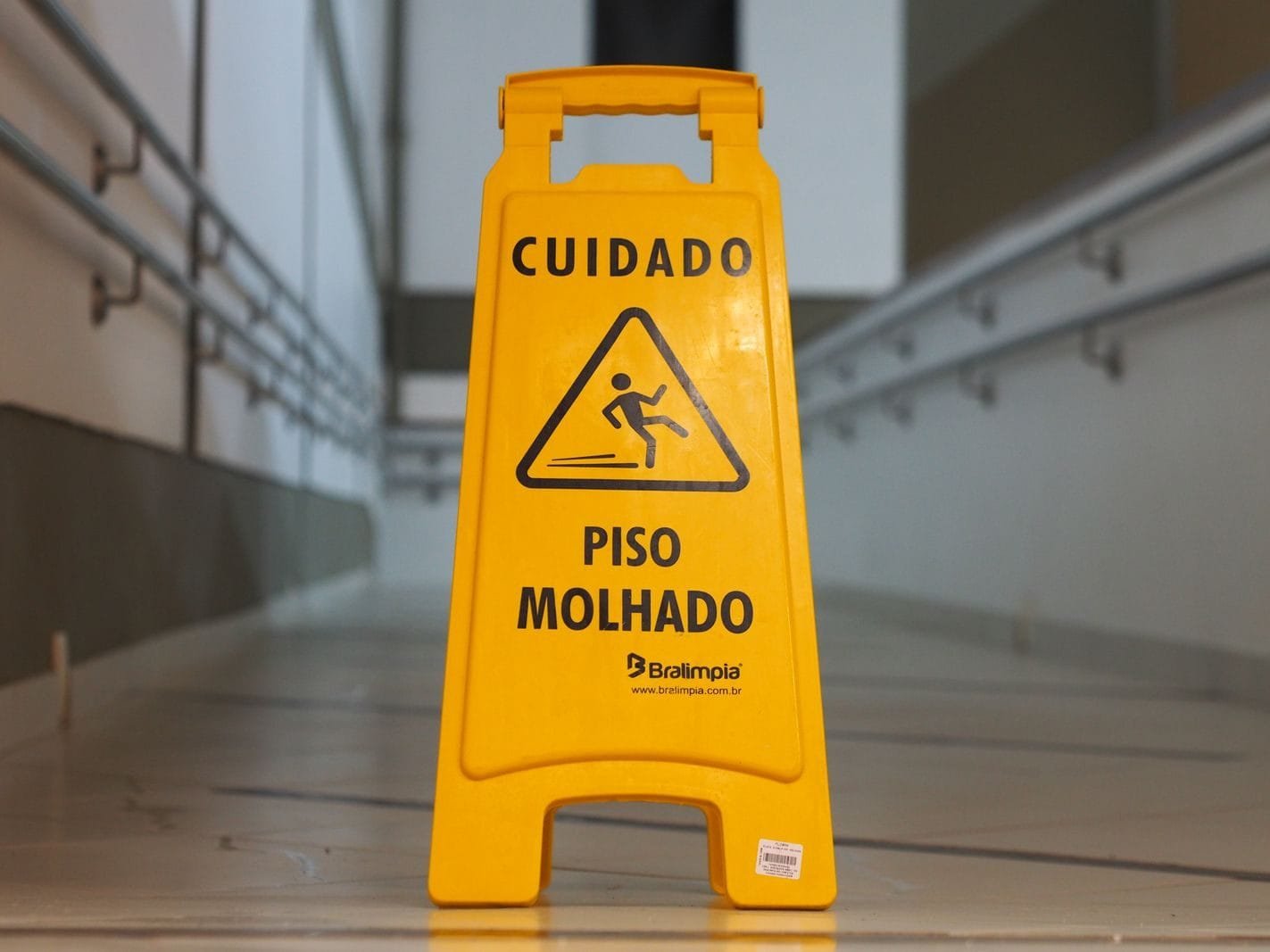 Responsabilidade Civil: Quando Você Pode Pedir Indenização 1 Bright yellow caution sign signals wet floor in a corridor with tiled flooring.