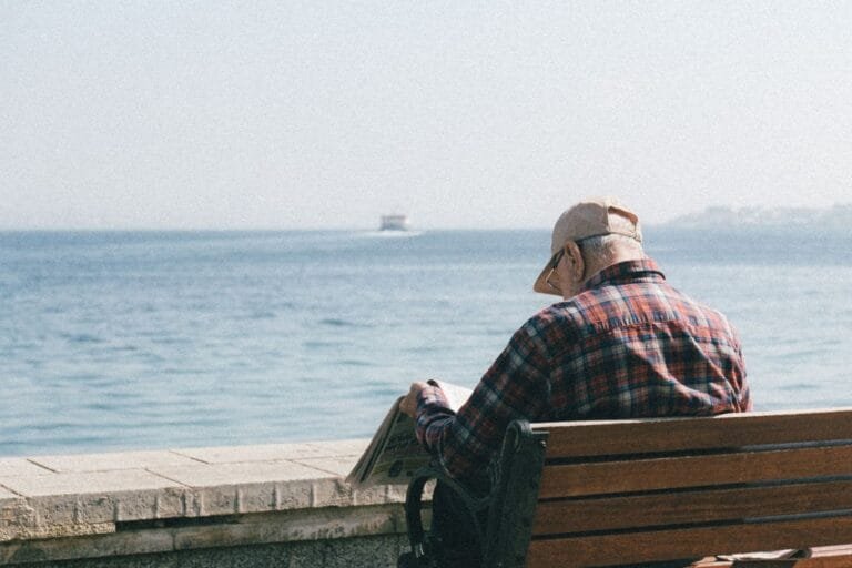 Senior man enjoys reading a newspaper while sitting by the seaside, embracing relaxation.