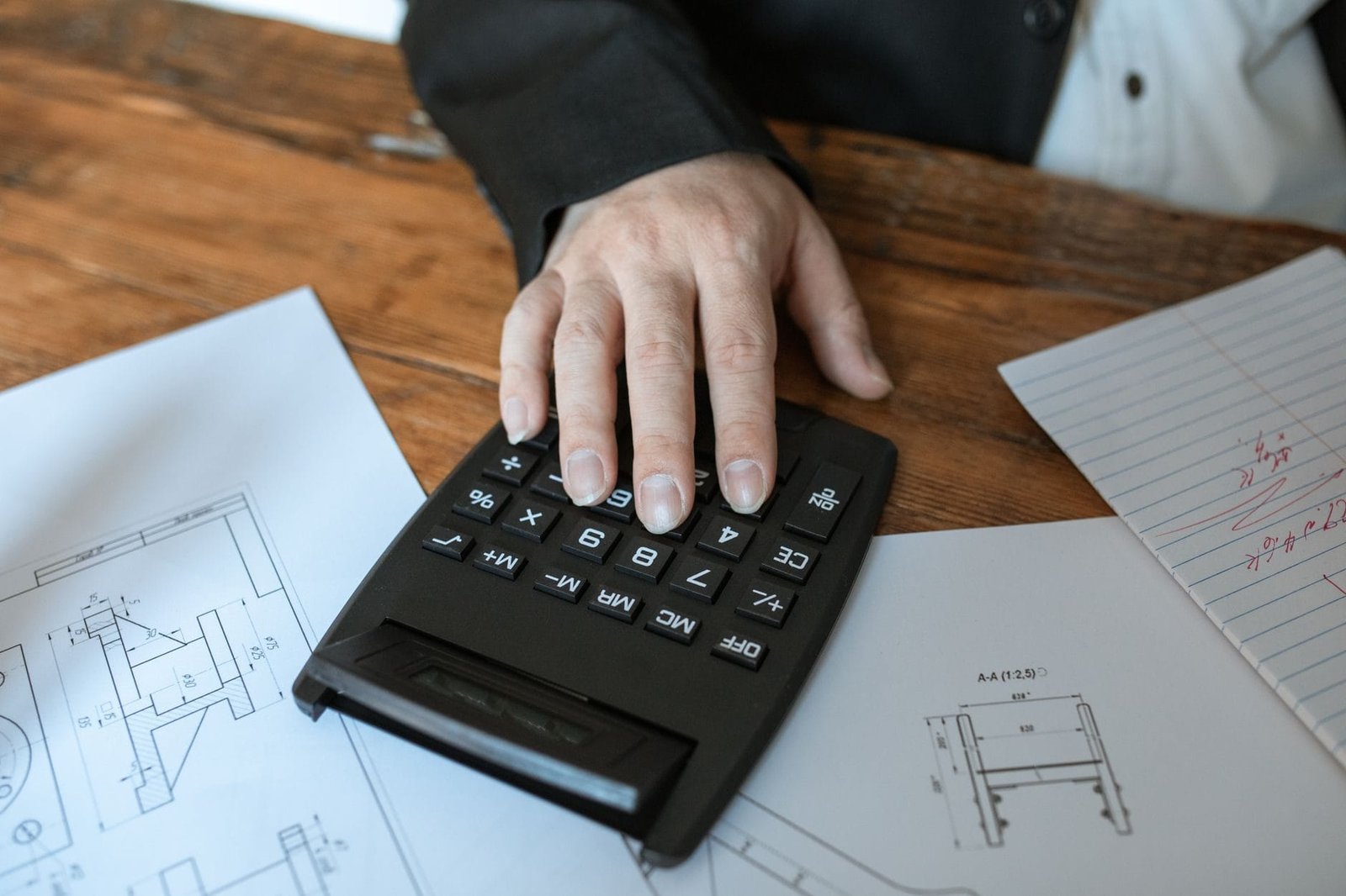 Revisao da vida toda: o que e a tese e quem pode ter interesse em discuti-la 1 Hand using calculator for architectural calculations on blueprints.