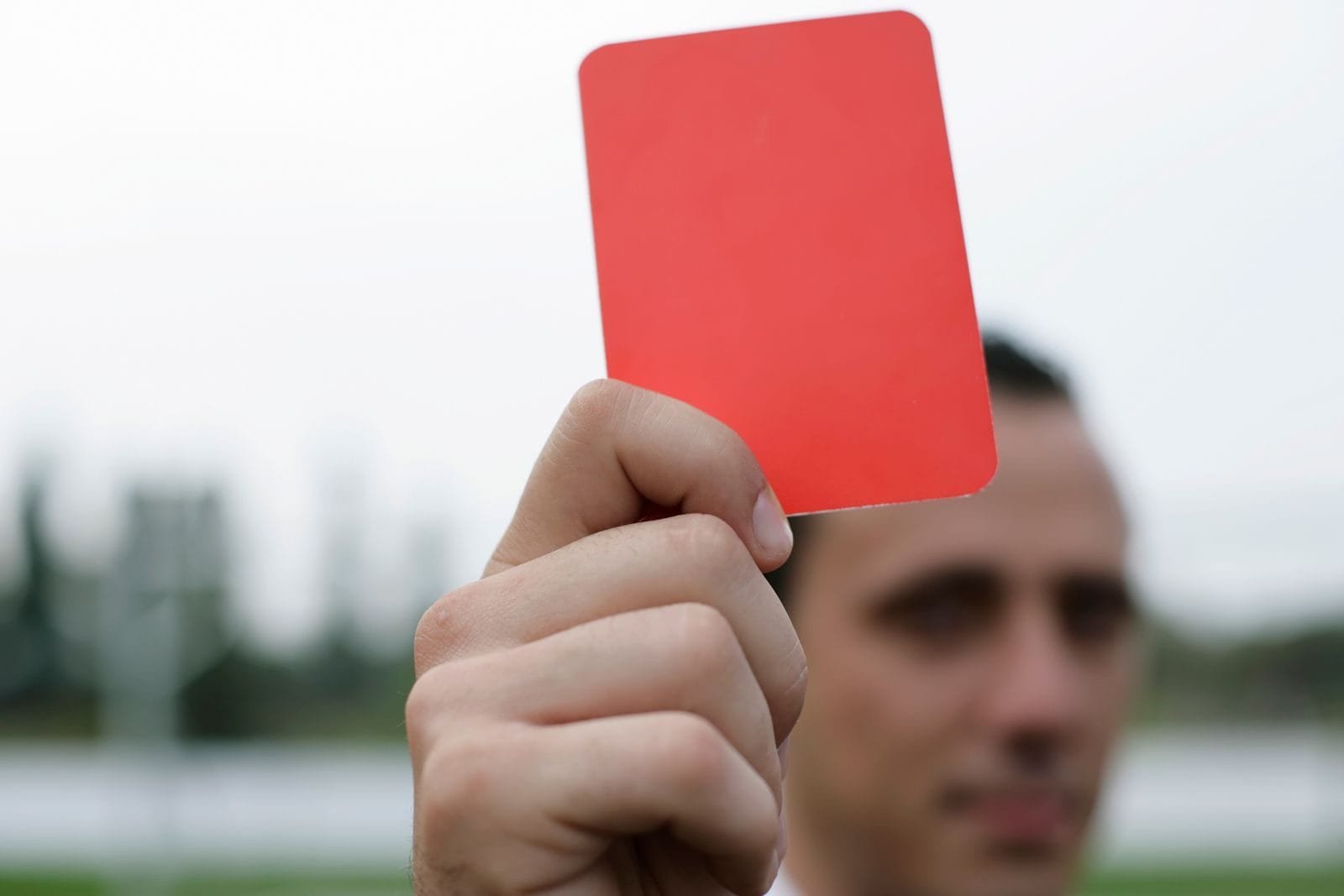 Sanções a empresas em licitações: advertência, multa e impedimento de contratar 1 Close-up of a referee holding a red card, signaling a penalty in a soccer match.