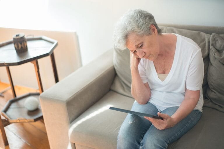 STF cancela em definitivo a tese da revisão da vida toda do INSS, por 8 votos a 3, com modulação de efeitos (novembro de 2025, Agência Brasil) 4 A senior woman sits thoughtfully on a sofa in a bright living room, holding a tablet.
