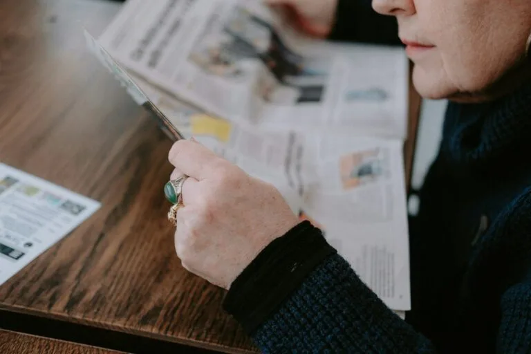 a woman sitting at a table reading a newspaper