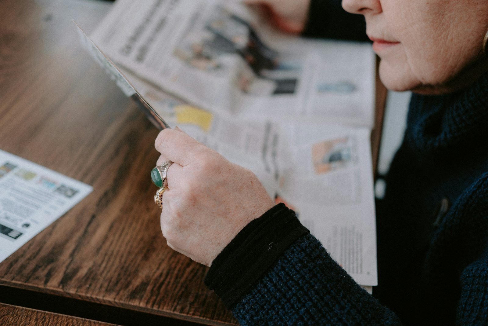 a woman sitting at a table reading a newspaper