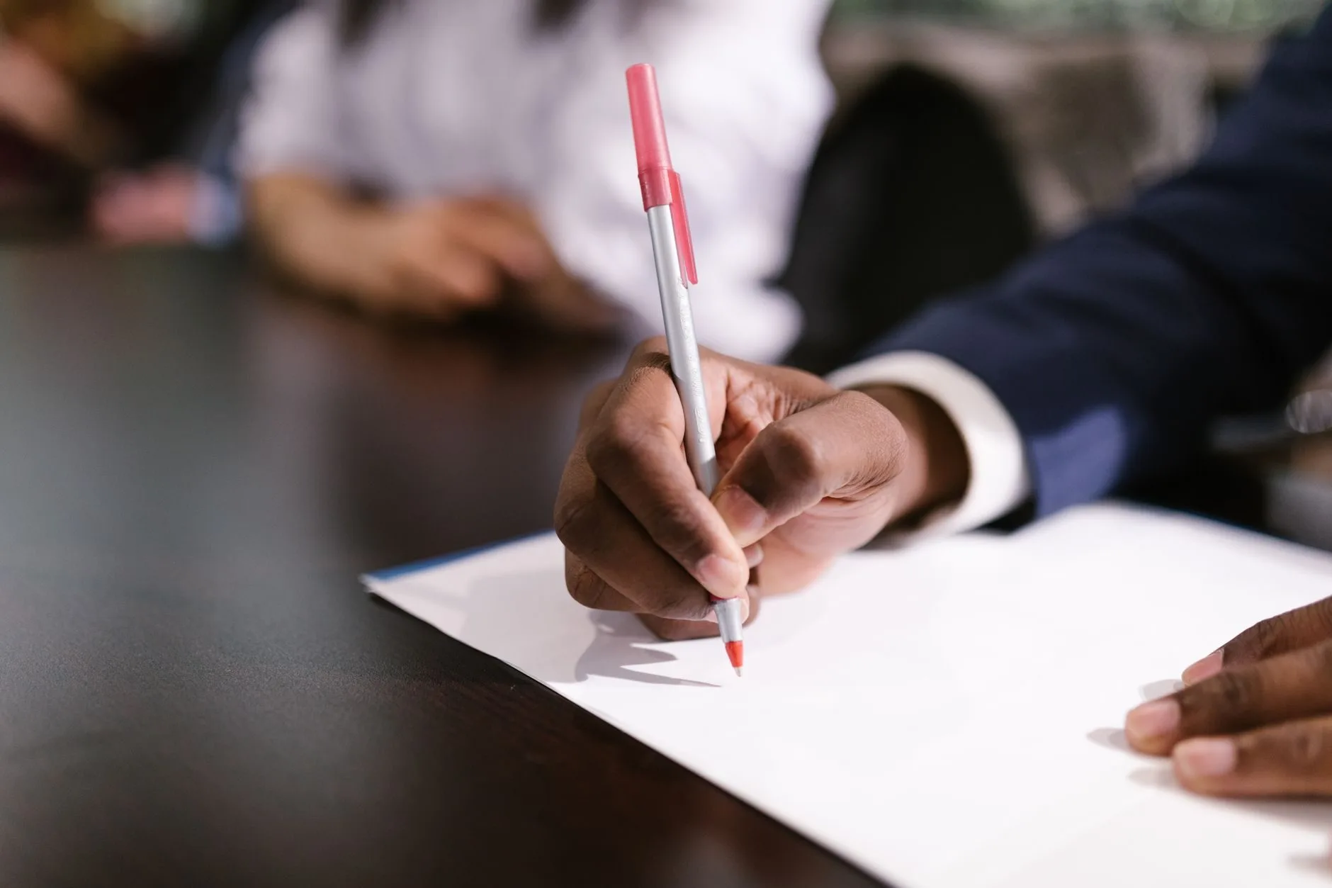 STJ fixa no Tema 1.124 os critérios de interesse de agir e o termo inicial dos efeitos financeiros de benefício previdenciário concedido com base em prova nova 1 An individual writing on white paper in a professional setting, focusing on the hand and p