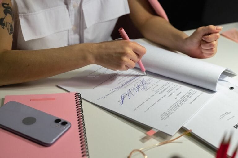 Close-up of a person writing on documents at a well-organized office desk.