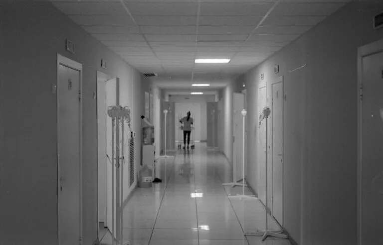 Tempo Especial do Profissional de Saúde (Enfermeiro, Médico, Dentista) 2 Monochrome image of a hospital hallway with a nurse in the background, highlighting healthcare environment.