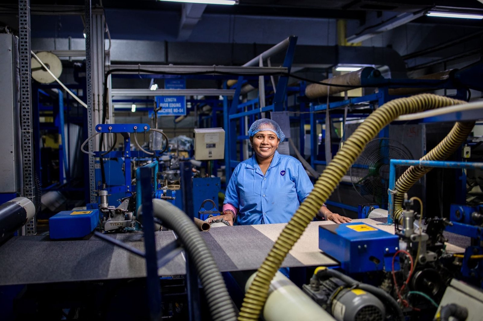 A female worker in a blue uniform smiles while working at a textile factory, surrounded by