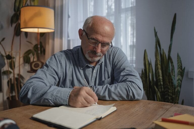 Testamento: Tipos, Validade e Como Fazer: Guia Atualizado 2 A senior adult man writing in a notebook at a desk in a cozy home office setting.