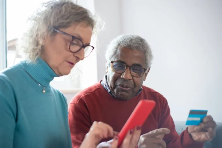 Teto do INSS Sobe Para R$ 8.475,55 com Reajuste de 3,9% 4 Elderly couple using smartphone and credit card for online shopping indoors.