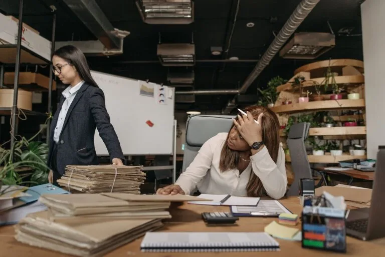 Teto remuneratório do servidor e as parcelas que ficam de fora 2 Two women working with documents in a modern office setting, one sitting at the desk, the other standing.