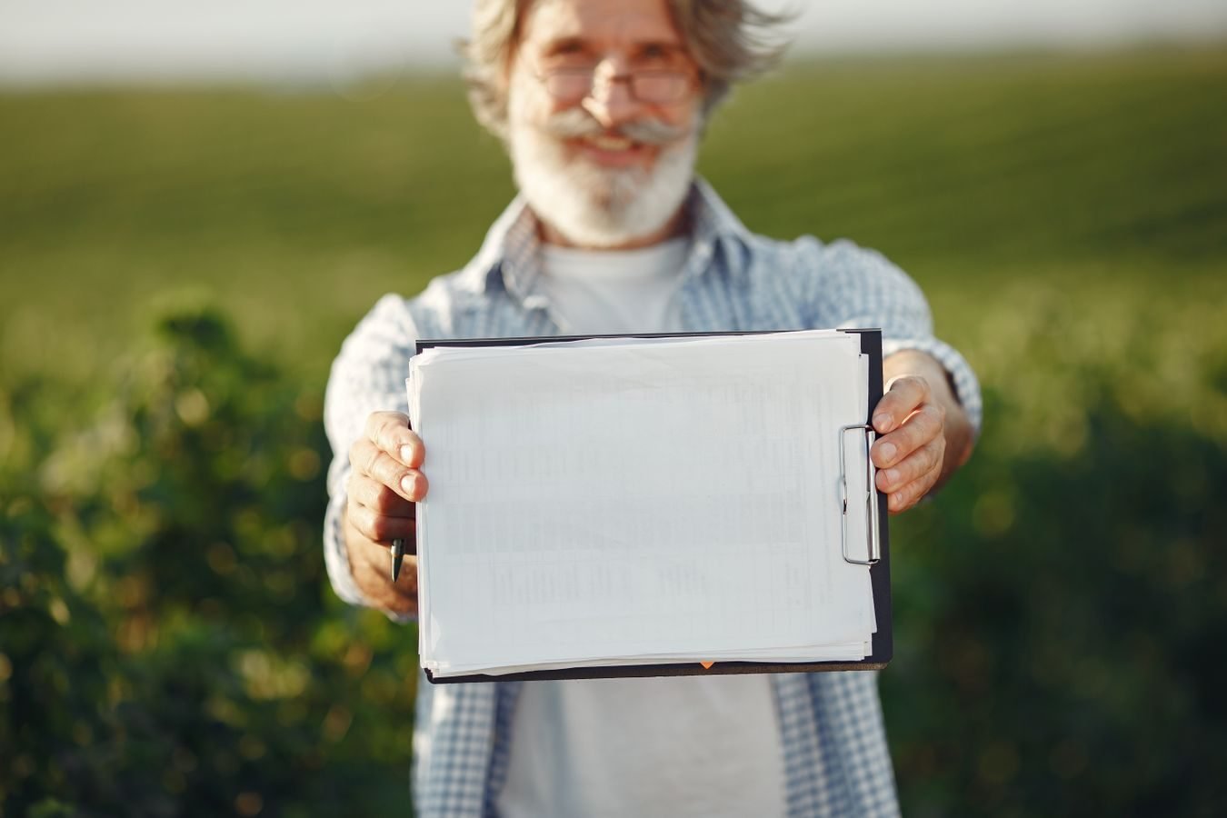 TNU reconhece certidao eleitoral com profissao rural e declaracao de sindicato (mesmo sem homologacao do INSS) como inicio de prova material de segurado especial rural 1 Bearded senior man with glasses holding a clipboard in a green field on a sunny day.