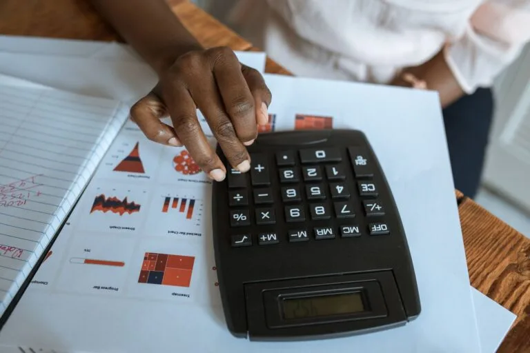 Person using calculator on desk with financial charts and graphs, ideal for business and f