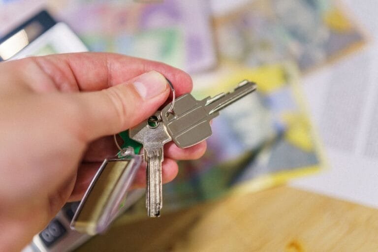 Como podemos ajudar? 2 Close-up of keys in hand representing property ownership with blurred financial documents in the background.
