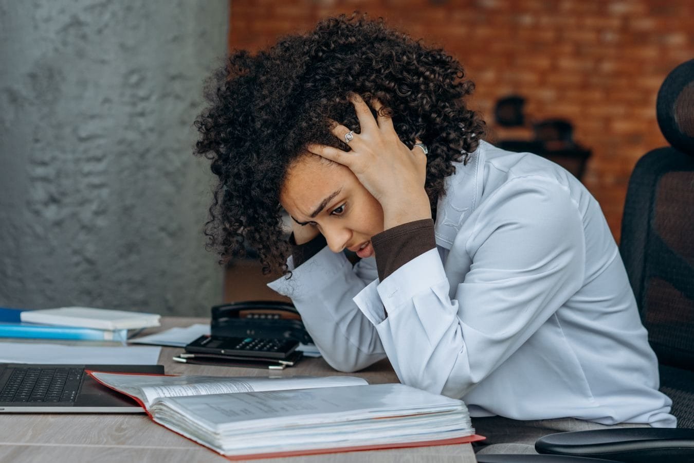 Transtorno mental grave do bancário e a aposentadoria por incapacidade 1 Woman sitting at desk appearing stressed while reviewing documents in an office setting.