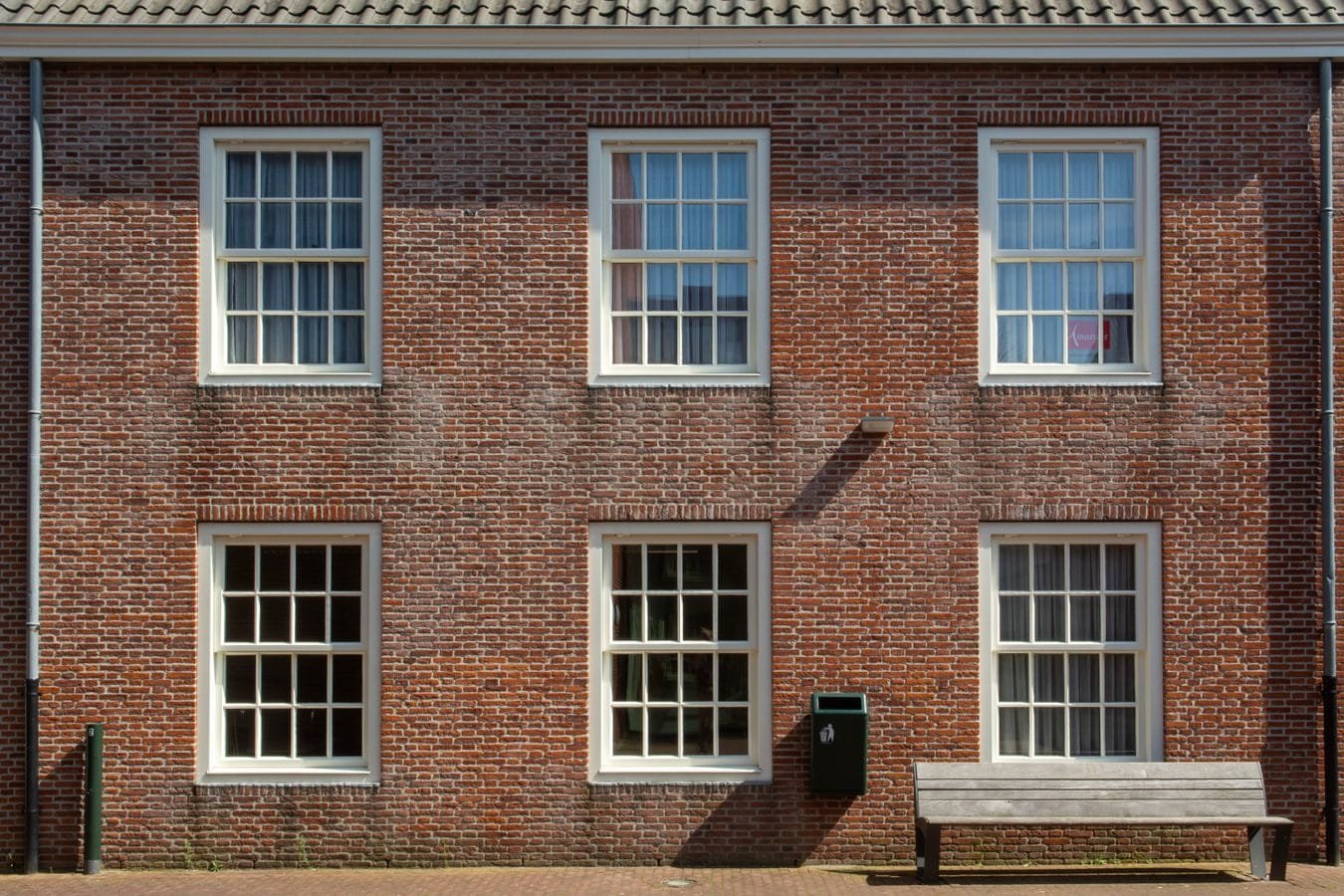 Usucapião de imóvel urbano: quando a posse vira propriedade 1 Front view of a brick building facade with sash windows and a wooden bench.