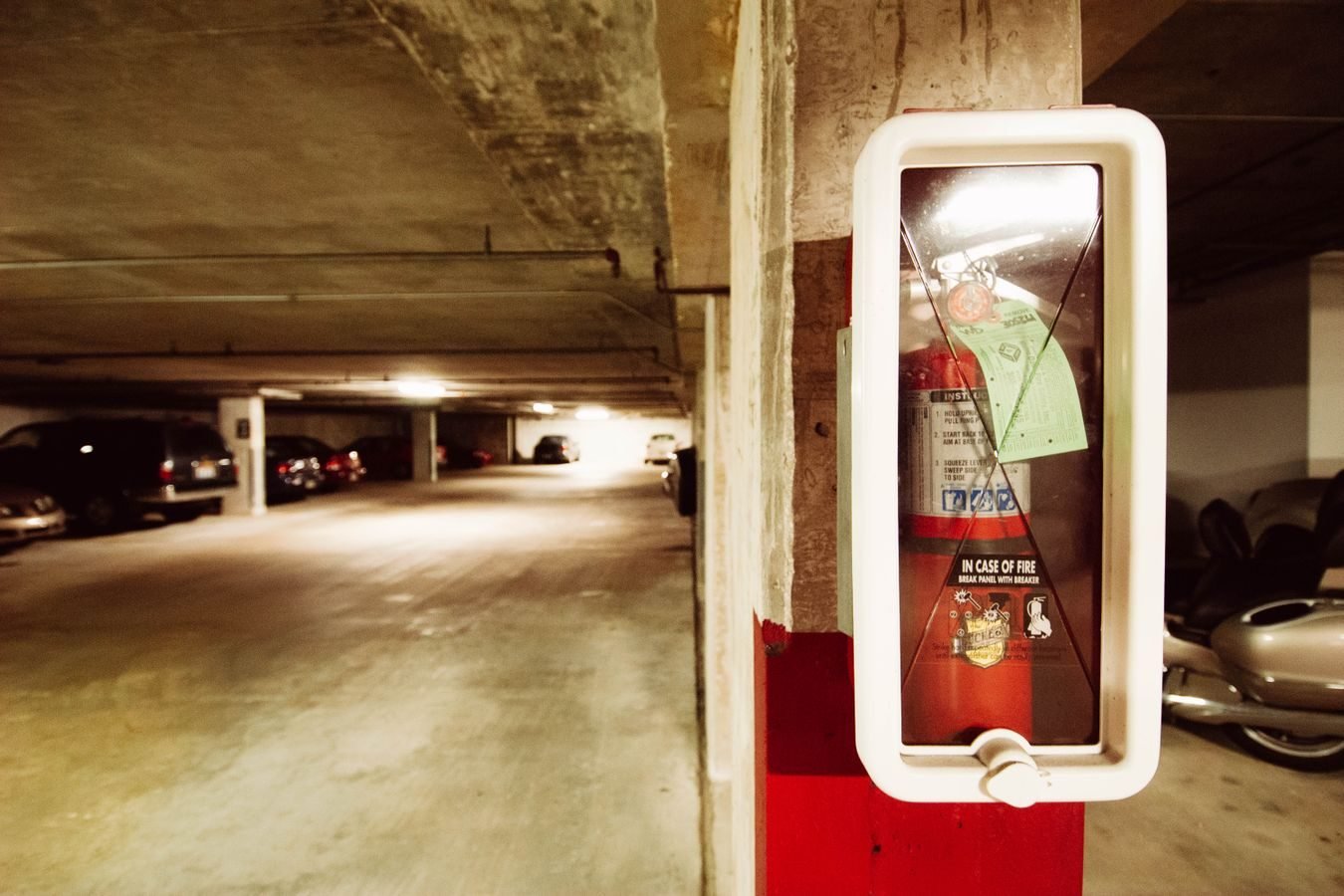 Fire extinguisher in an underground parking garage with parked cars.