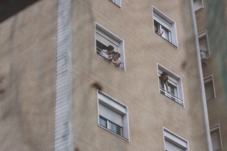 People looking out from windows in a city apartment building showing urban life.