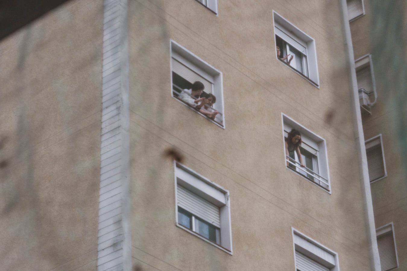 Vizinho Barulhento: Medidas Legais que Você Pode Tomar 1 People looking out from windows in a city apartment building showing urban life.