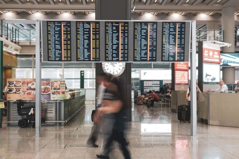 Como podemos ajudar? 11 Blurred motion of travelers in a modern airport terminal with departure screens and a prominent clock.