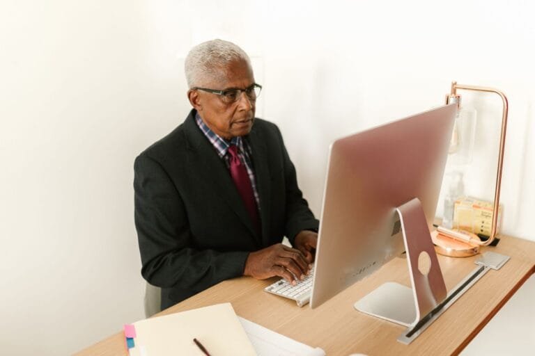 Senior man in corporate attire focusing on work at his desktop computer in a modern office