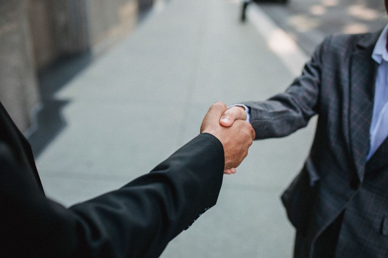 Como escolher entre acordo e processo judicial 1 Close-up of two businessmen shaking hands outside, symbolizing partnership and agreement.