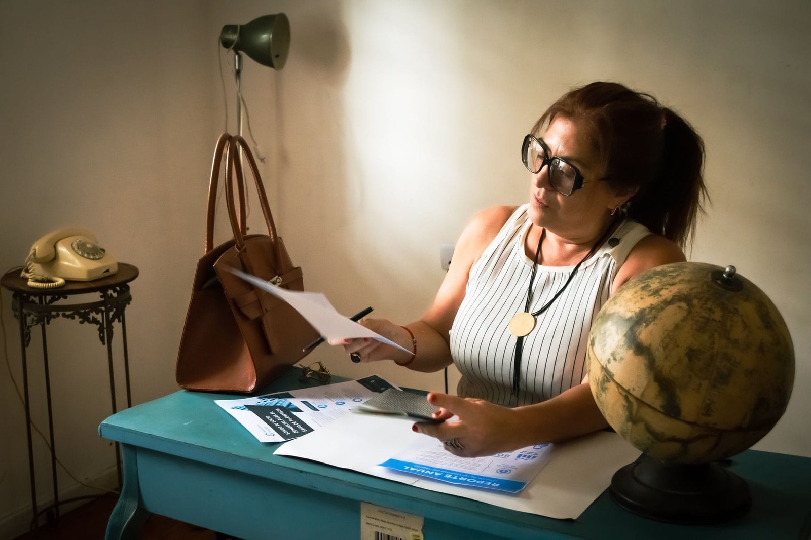 Woman analyzes documents at a vintage desk with a globe, creating a cozy workspace ambianc
