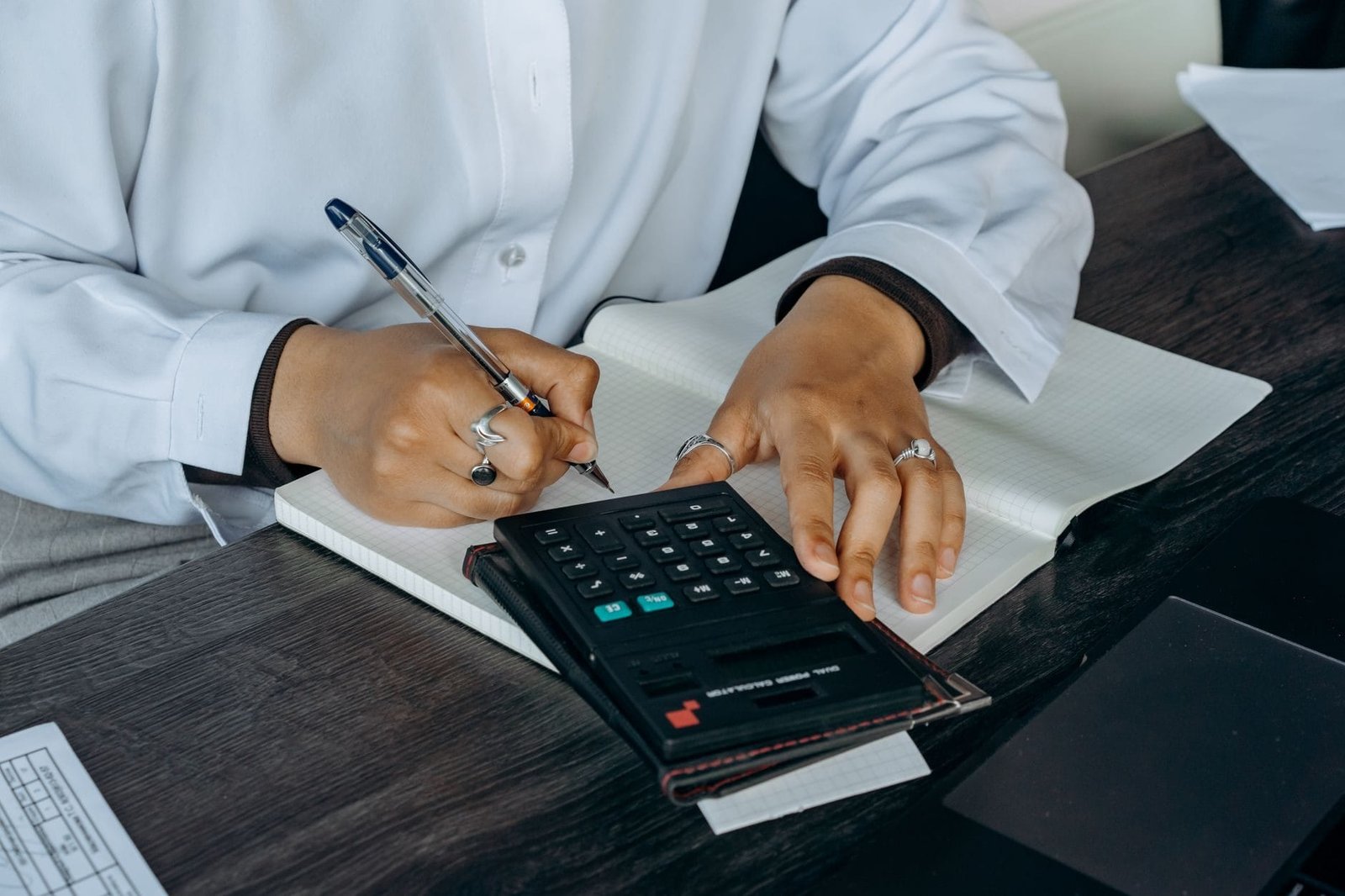 Close-up of a professional writing notes with calculator at a wooden desk.