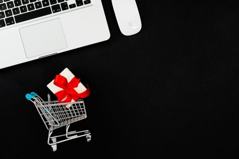 Minimalist image of a shopping cart with a gift on a black background beside a laptop, ide