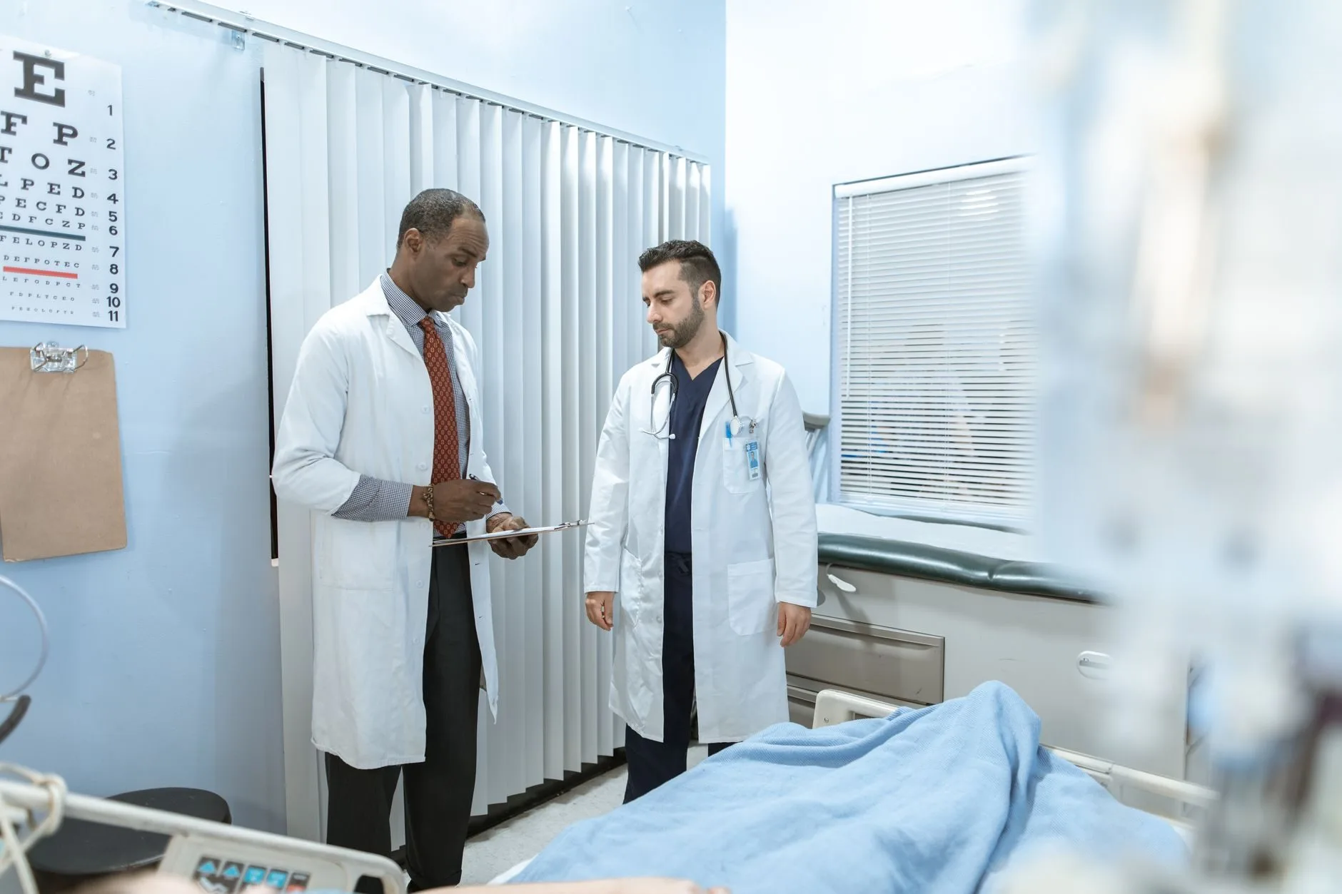 Doença preexistente pode impedir o benefício do INSS 1 Two doctors review a patient's chart in a hospital room, focusing on healthcare cooperatio