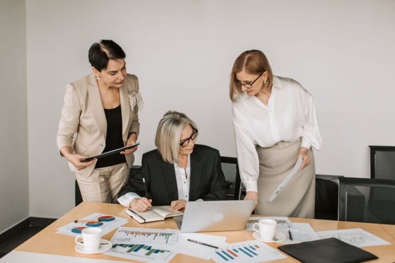 Sociedade limitada como proteger o patrimônio pessoal 1 Three businesswomen discussing documents during a meeting in a modern office setting.