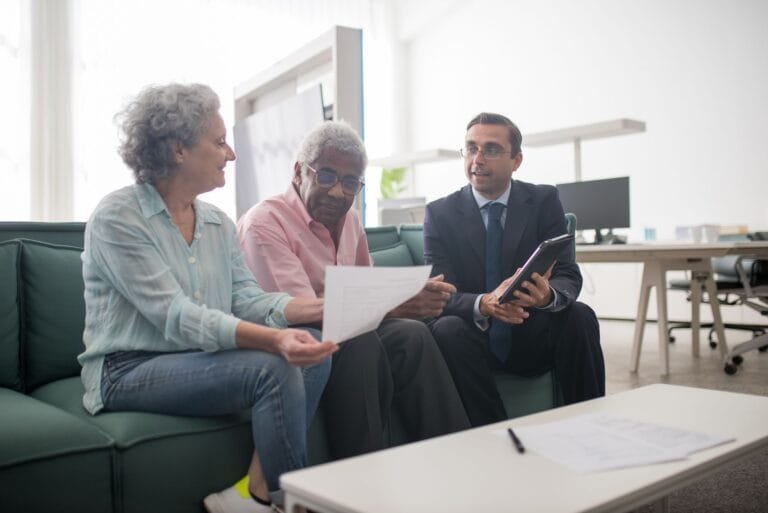 BPC/LOAS na revisão de 2026: como o beneficiário mantém o benefício e evita o cancelamento indevido 5 Senior couple discussing documents with a business advisor in a modern office setting.