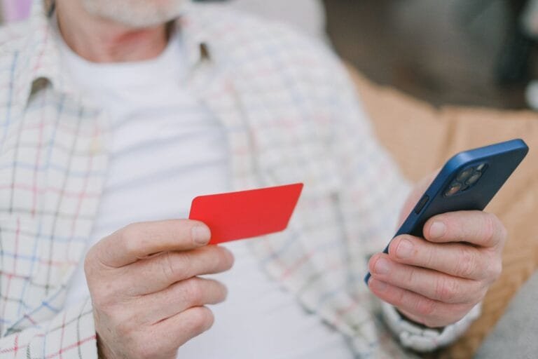 Pessoa idosa utilizando celular e cartão em operação digital